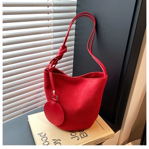 Détail du sac seau en daim rouge avec sangle nouée et porte-monnaie rond sur des livres