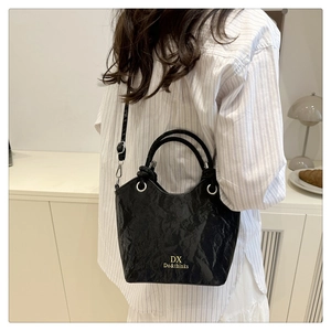 Détail d'un sac seau noir texturé avec logo doré porté par un mannequin dans un intérieur