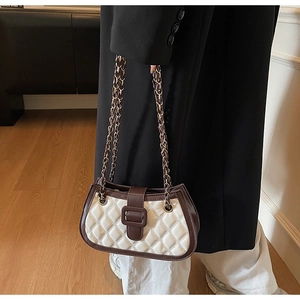 Dettaglio borsa trapuntata bianca con bordo marrone e tracolla dorata su un cappotto
