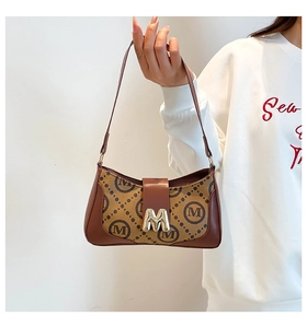 Detailed close-up of brown baguette bag with monogram print and golden metal M buckle