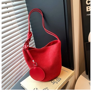 Gros plan d'un sac seau rouge en daim avec bandoulière nouée et breloque porte-monnaie