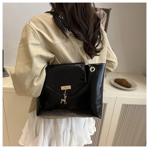 Detail of black patent leather shoulder bag featuring a gold deer charm and chain strap