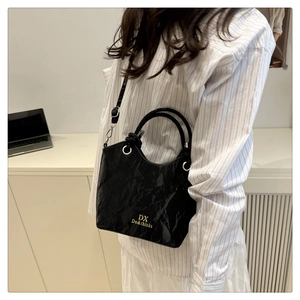 Détail d'un sac à main noir en cuir verni froissé avec logo doré et anneaux argentés