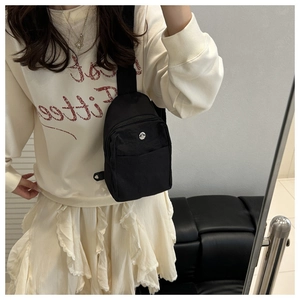 Close-up of black nylon crossbody bag with circular metal logo and front zipper detail