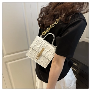 Detail of white embossed leather handbag with gold chain strap and metallic clasp on model