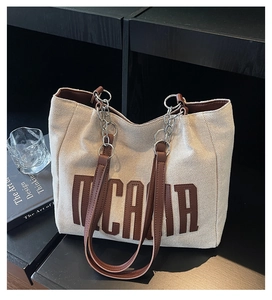 Detail of canvas tote bag with brown leather letter patch and metal chain strap