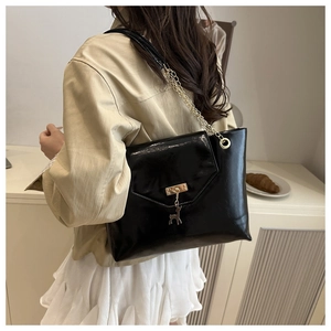 Detail of glossy black leather handbag with gold deer pendant and chain strap on a model
