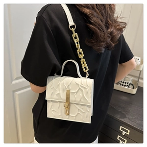 Detail of white embossed texture shoulder bag with gold chain and metal buckle
