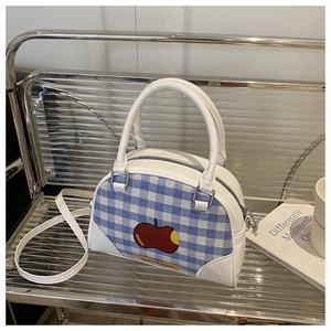 Close-up of blue plaid Boston bag with red apple print and white faux leather straps