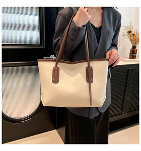 Detail of minimalist beige tote bag with brown straps worn by a model in a suit