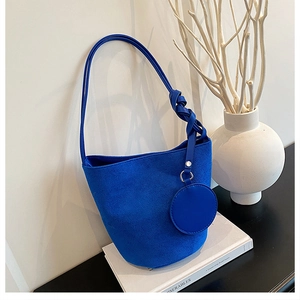 Détail du sac seau en daim bleu roi avec bandoulière nouée et breloque ronde sur des livres