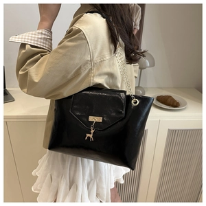 Detail of black patent leather tote with gold chain strap and deer charm pendant