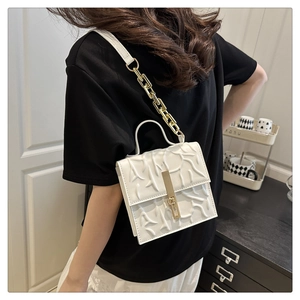 Detail of white crossbody bag with geometric texture and golden chain strap on model
