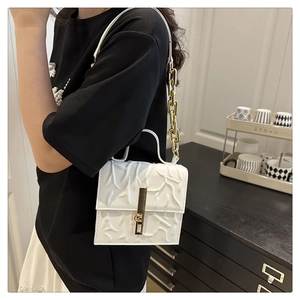 Detailed macro view of white embossed leather handbag with gold buckle and chain strap