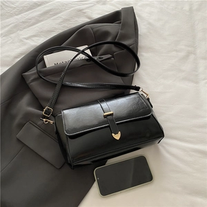Sac bandoulière rétro en cuir brillant noir avec boucle cœur dorée sur fond de veste grise