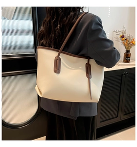 Detail of a large beige tote bag with brown trim worn by a model in a cozy indoor setting