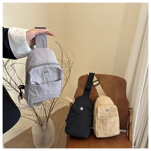 Nylon crossbody bags in grey black and beige displayed on a wooden chair setup