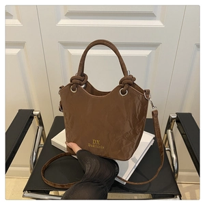 Détail d'un sac seau en cuir marron texturé avec poignée et logo doré sur des livres blancs