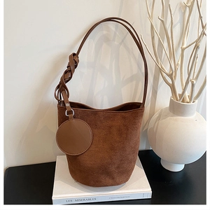 Détail du sac seau en daim marron avec bandoulière tissée et pendentif porte-monnaie