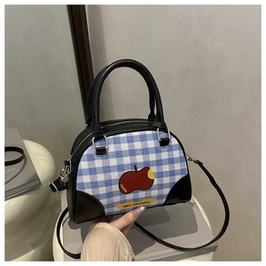 Detail of blue plaid boston bag featuring red apple print and black leather accents
