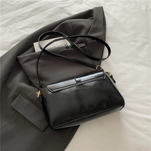 Sac à bandoulière minimaliste en cuir noir brillant avec boucles dorées sur blazer
