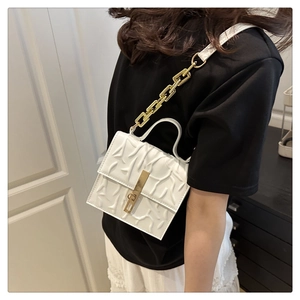 White crossbody bag with embossed texture and gold chain strap worn by a model