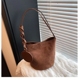 Détail d'un sac seau en daim marron foncé avec une anse tressée et un pendentif décoratif