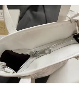 Detail view of smooth silver zipper and deep red interior lining of white bucket bag