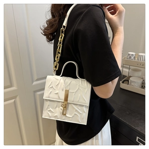 Detail of white embossed shoulder bag with gold chain strap and textured leather finish