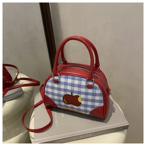 Detail of red leather and blue plaid canvas handbag with cute apple patch and strap
