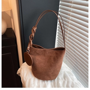 Détail du sac seau en daim marron avec bandoulière en cuir tressé sur un tissu en dentelle