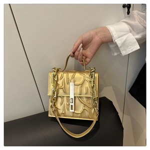 Close-up of golden square handbag with branch-like texture and metallic chain strap