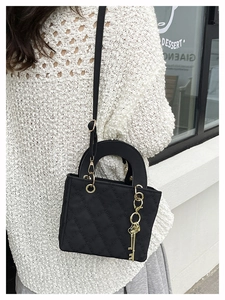 Detail of black quilted crossbody bag with gold key pendant and elegant top handle