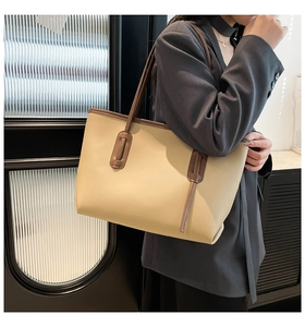 Close-up of beige tote bag with brown straps worn by a model in a professional office setting