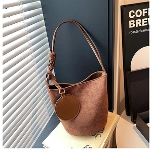 Détail d'un sac seau en daim marron avec bandoulière tissée torsadée et pendentif rond chic