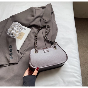 Close-up of semi-circular dark brown leather chain bag on a stylish white bedding background
