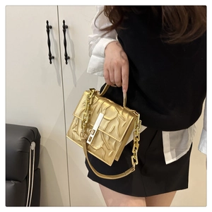 Detail of golden crossbody bag with wavy embossed texture and metal chain strap