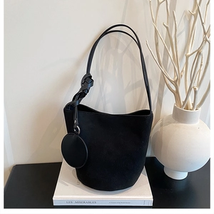 Gros plan du sac seau en daim noir avec petit porte-monnaie sur un décor minimaliste élégant