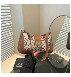 Detail of vintage patterned shoulder bag with metal M-logo buckle and leather strap