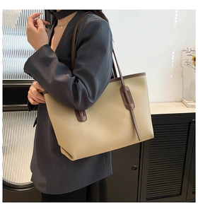 Model wearing a large beige tote bag with brown straps in a minimalist indoor setting