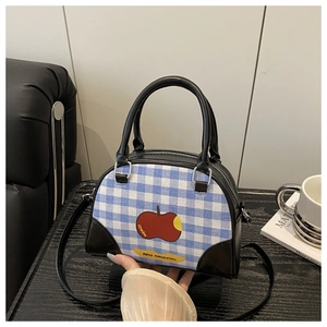 Close-up of blue plaid crossbody bag with red apple print and black leather handles