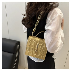Close-up of golden square crossbody bag with embossed texture and thick chain strap