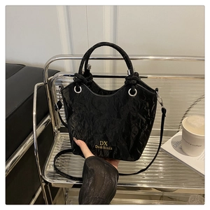 Détail d'un sac seau plissé noir brillant avec logo doré et finitions en métal argenté