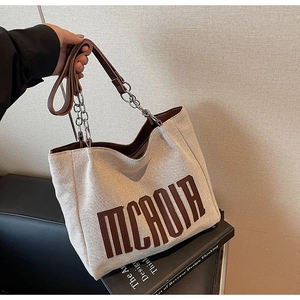 Detail of canvas tote bag showing MCHOIA logo and leather metal chain strap texture