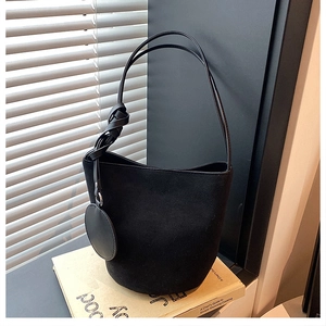 Détail d'un sac seau en suédine noire avec nœud coulissant et pendentif sur un livre