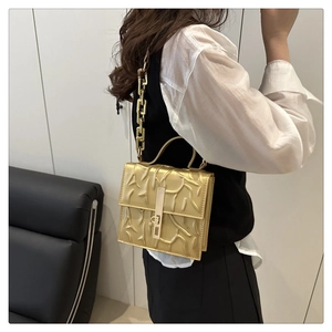Detail of a gold square bag featuring 3D embossed texture and chunky metal chain strap