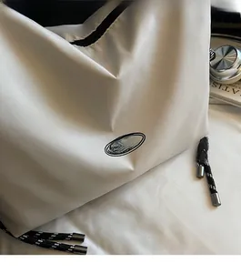 Detail showing the cream nylon fabric texture and logo of the crossbody bag