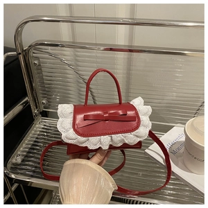 Close-up of red ballet-style handbag featuring white lace trim and bow on metal shelf