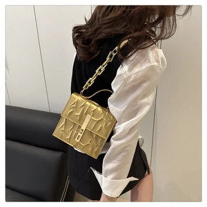 Close-up of golden square shoulder bag featuring chain strap and textured surface