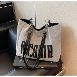 Detail of woven canvas tote bag featuring metal chain straps and brand text print